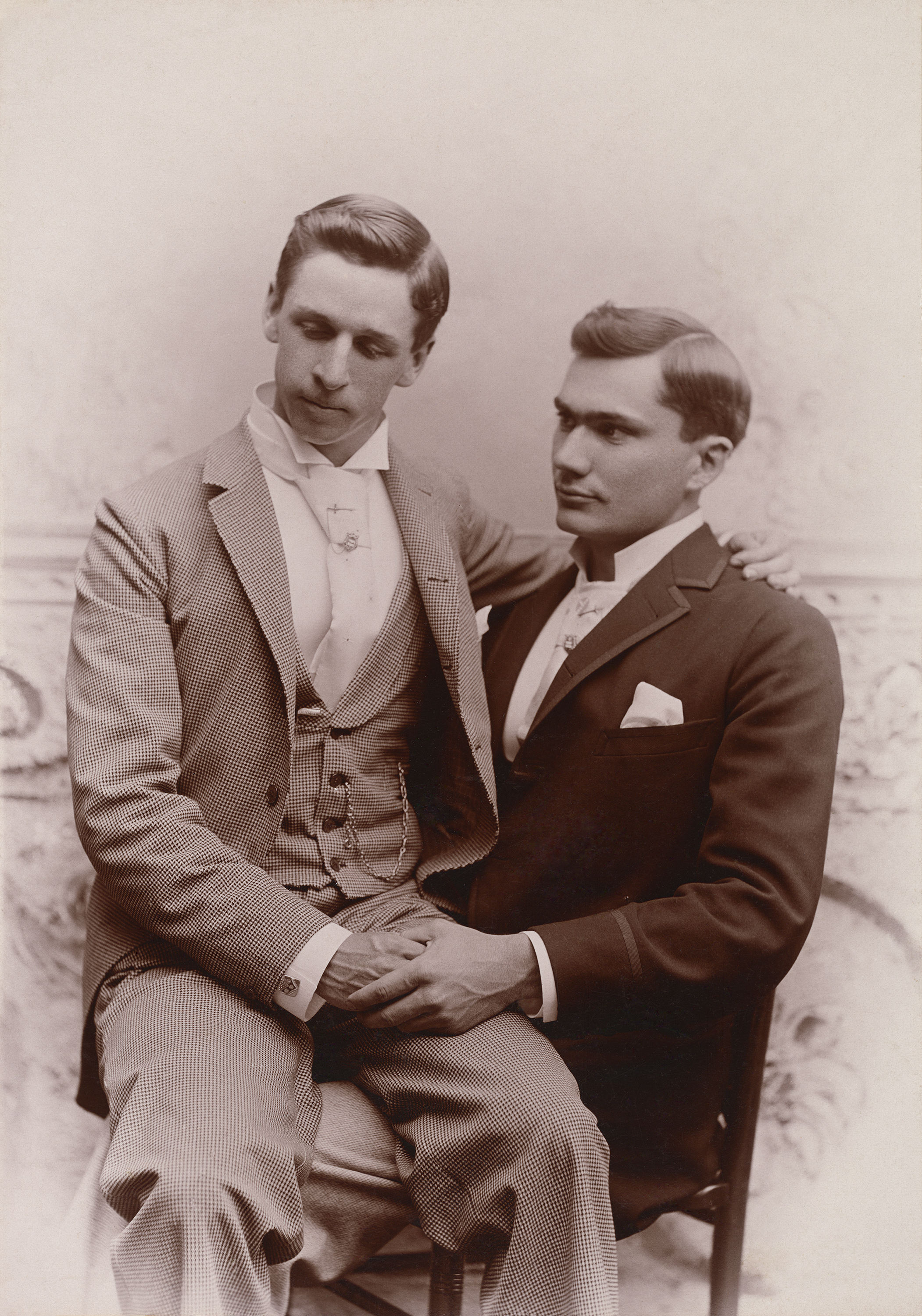Two men, one sitting on the other's lap in suits, Loving, a history of men in love through photographs