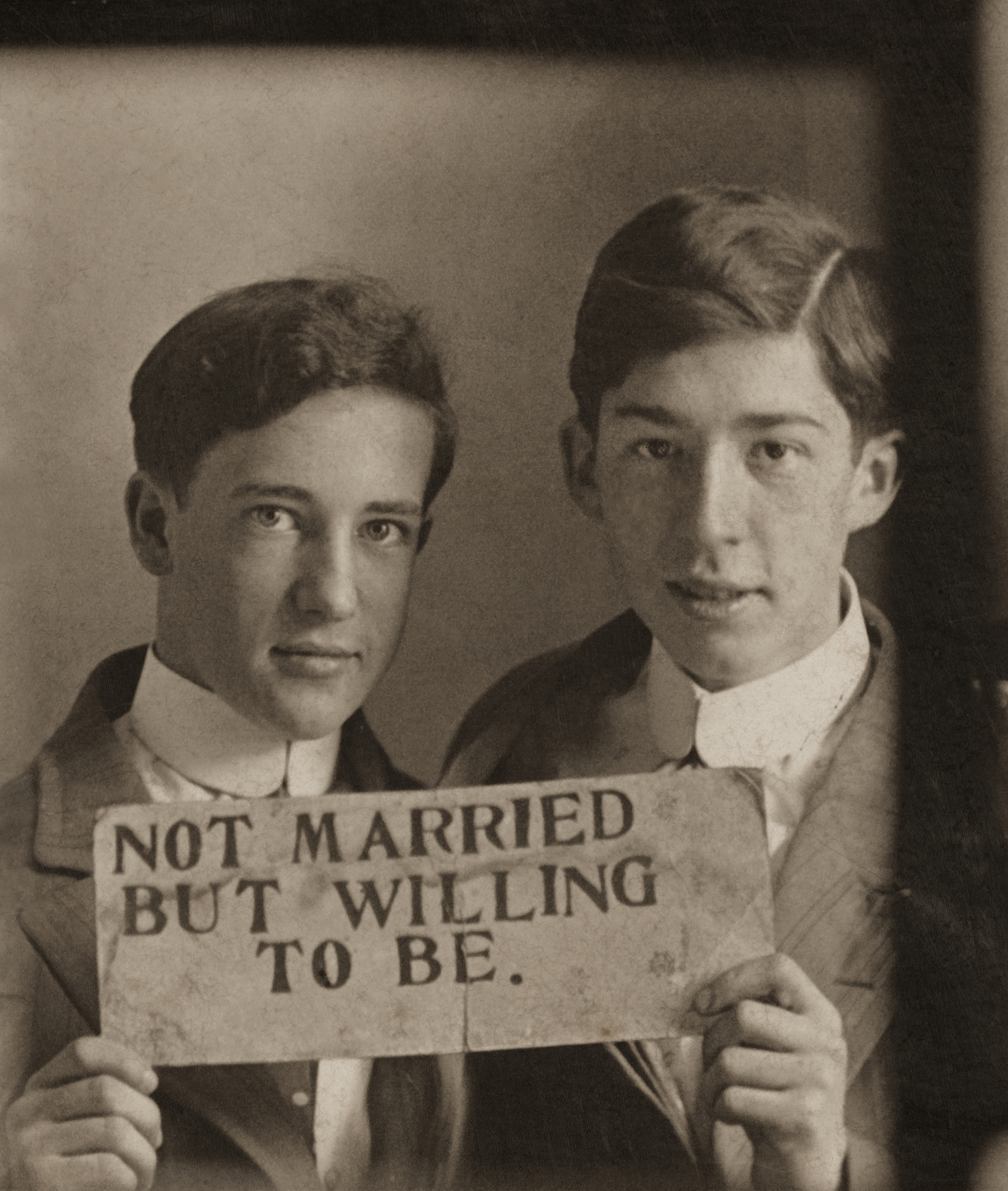 Two men in suits holding up a sign, "Not married but willing to be"