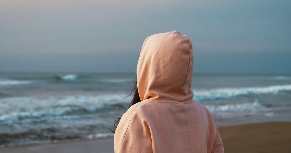 A woman with her hood pulled up stares at the sea