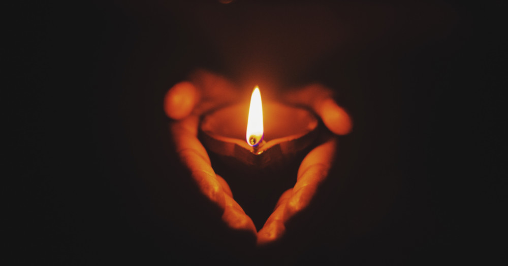 two hands holding a lit candle, transgender lives lost