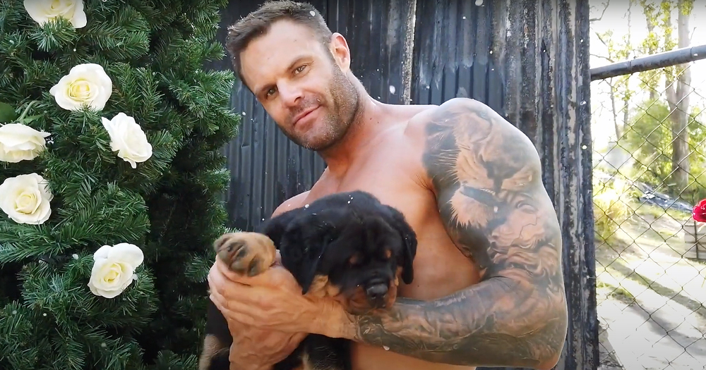 One of the Australian firefighters holding a puppy, shirtless, looking at the camera