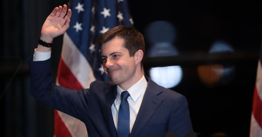 Pete Buttigieg smiling and waving in front of the U.S flag, he received a nomination in the presidential cabinet