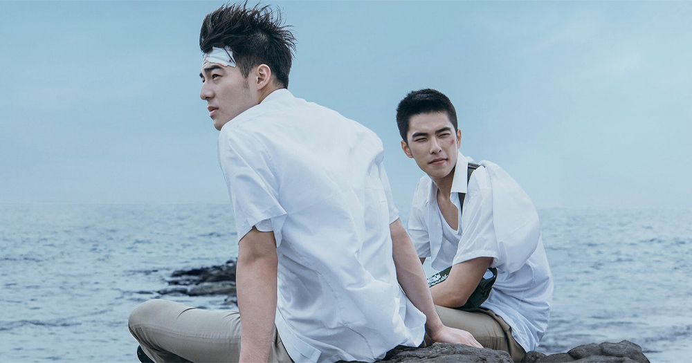 Two young men sit on a windy beach
