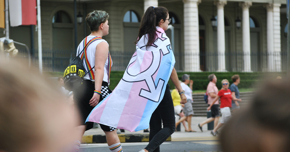 young people walking together, one wrapped in a trans flag