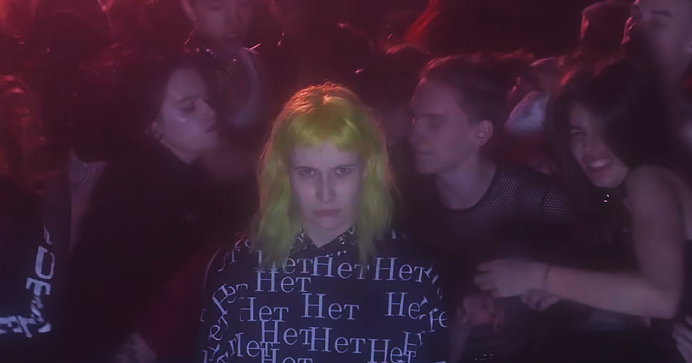 A still from RAGE music video showing members of Pussy Riot gathering around one person with yellow hair