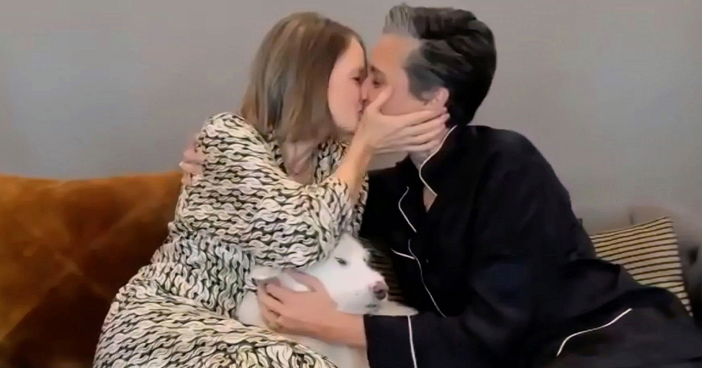 Two women kissing with a dog sitting between them