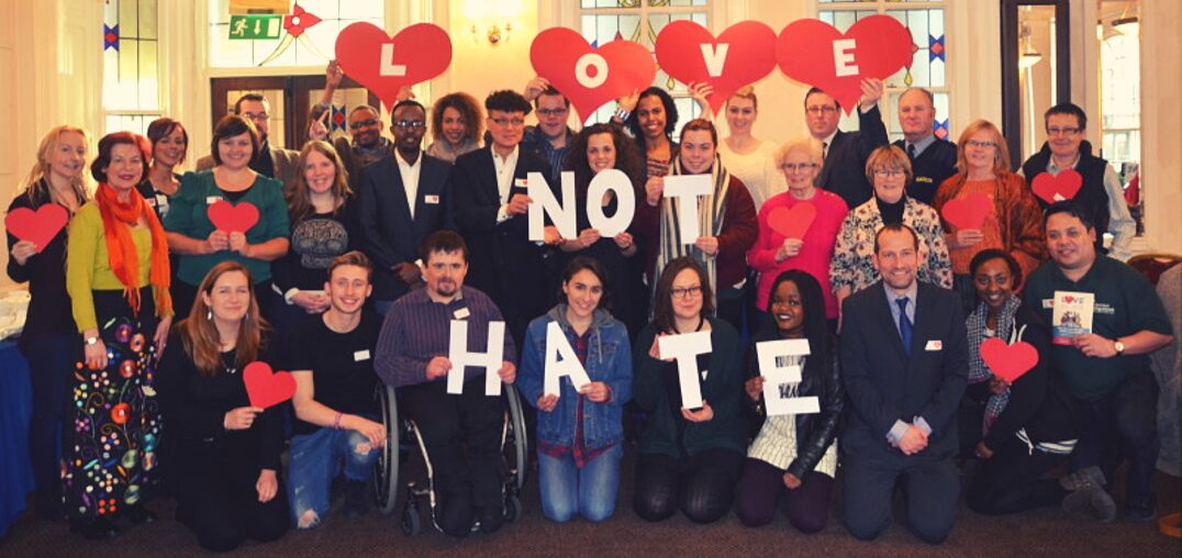 gathering of people holding up signs saying love not hate, calling for legislation against racist incidents