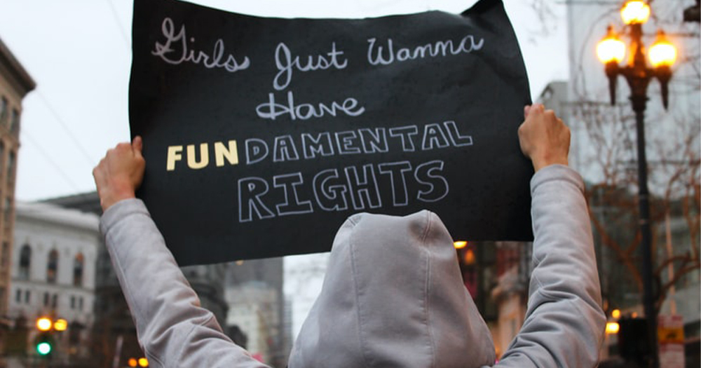 A woman seen from behind holding up a protest sign