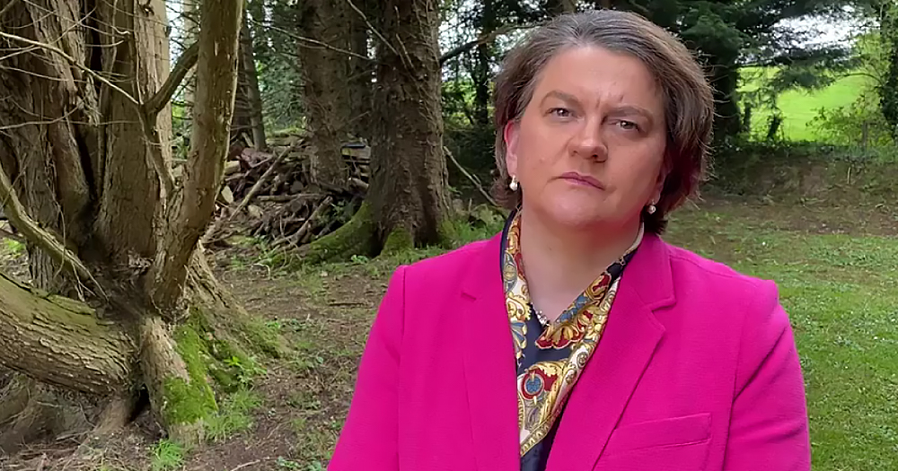 An annoyed looking woman in a suit stands in a forest