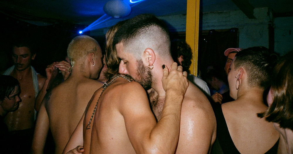 Two topless men embracing on a dance floor