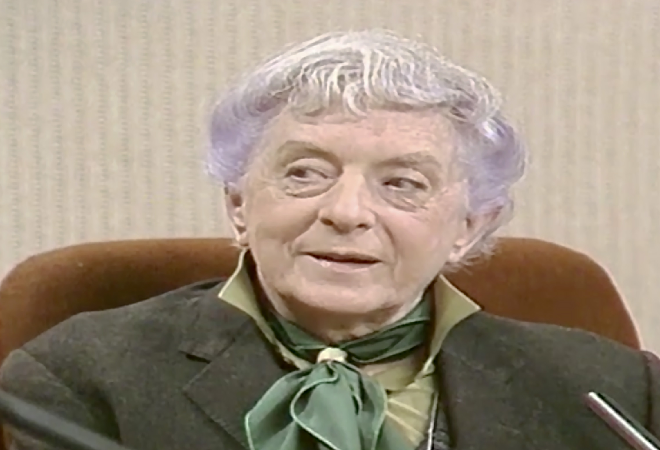 An elderly man wearing a green tie sits on a TV set