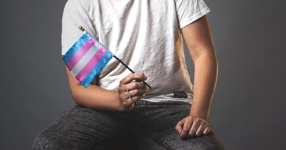 The torso of a man holding a trans flag