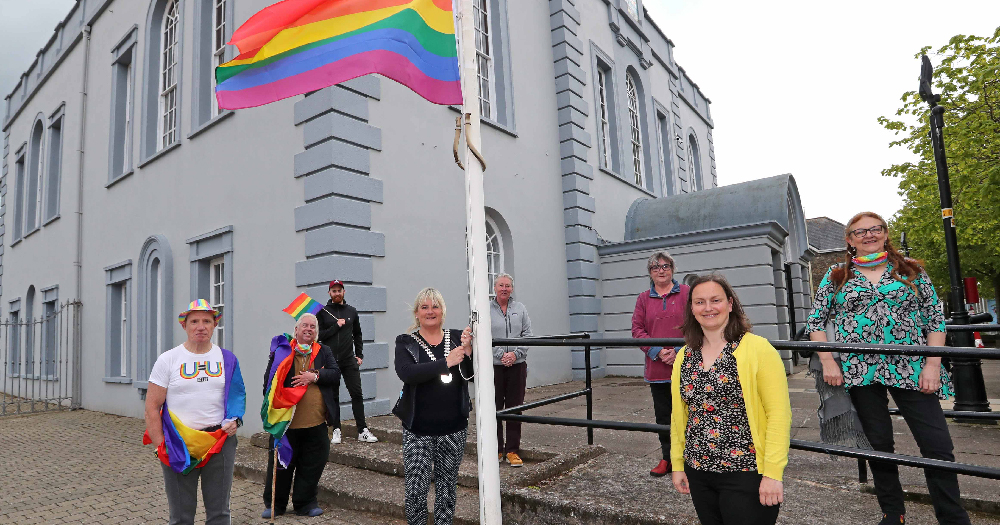 A group of people raising a rainbow flag on a flagpole