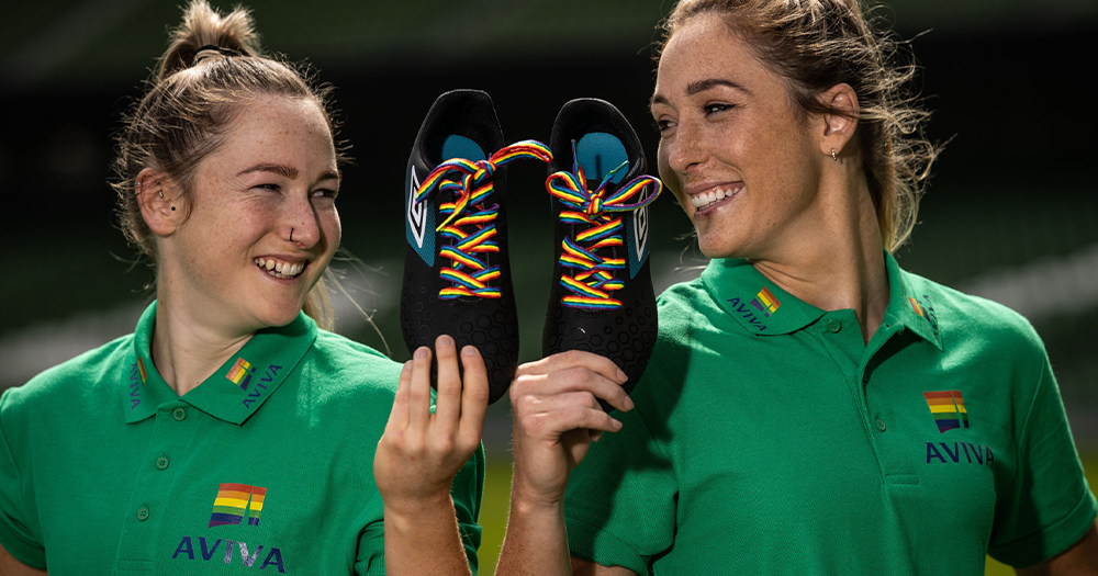 Two smiling sportswomen holding up boots with rainbow laces
