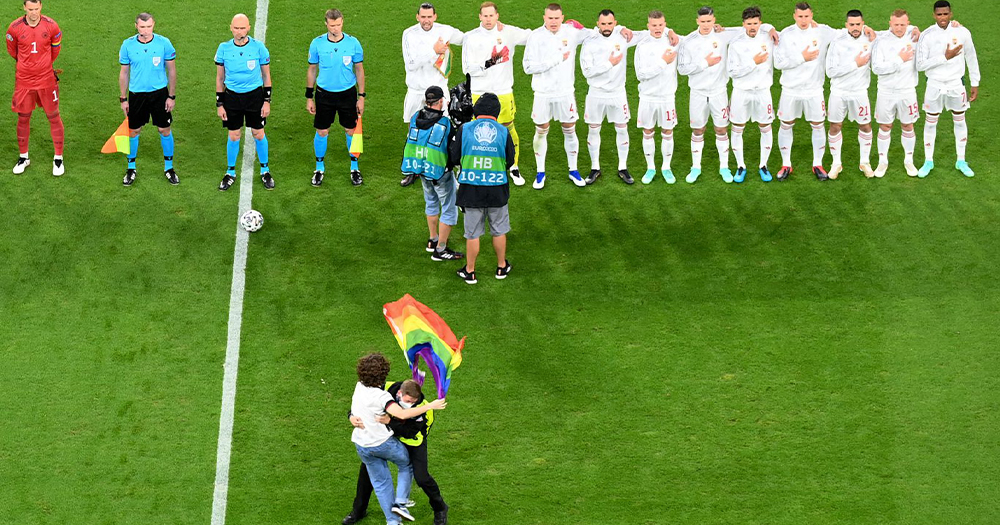 A protestor invading a football match with a Pride flag gets stopped by security