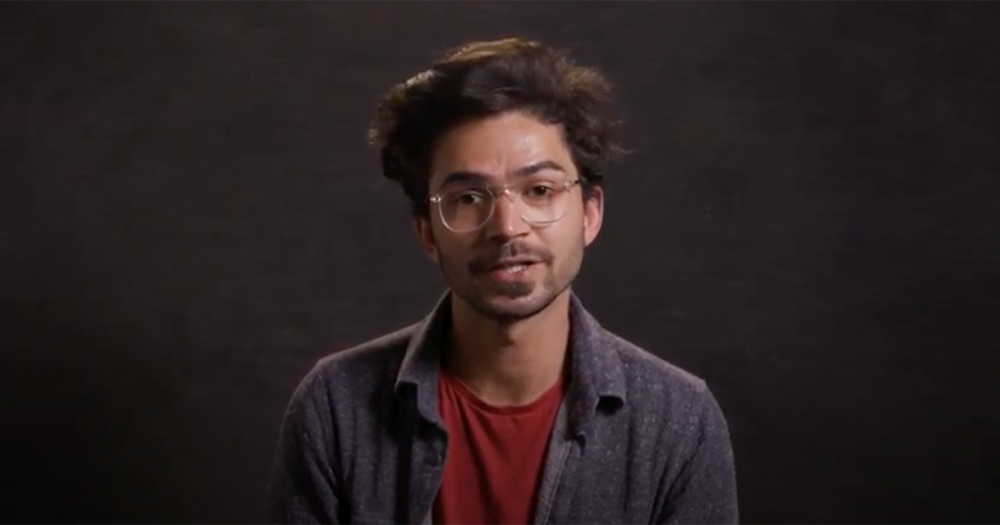 A bearded young man with glasses speaks to the camera