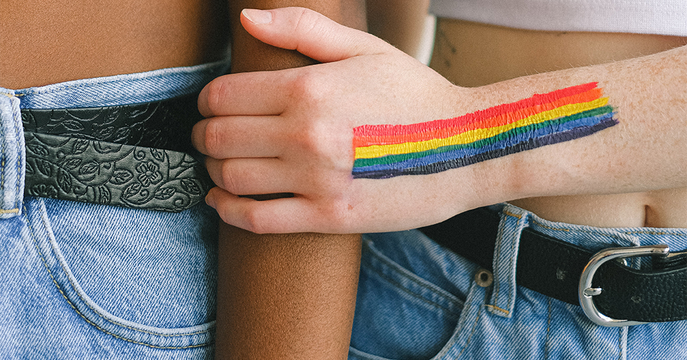A hand with a rainbow painted on it holds another arm