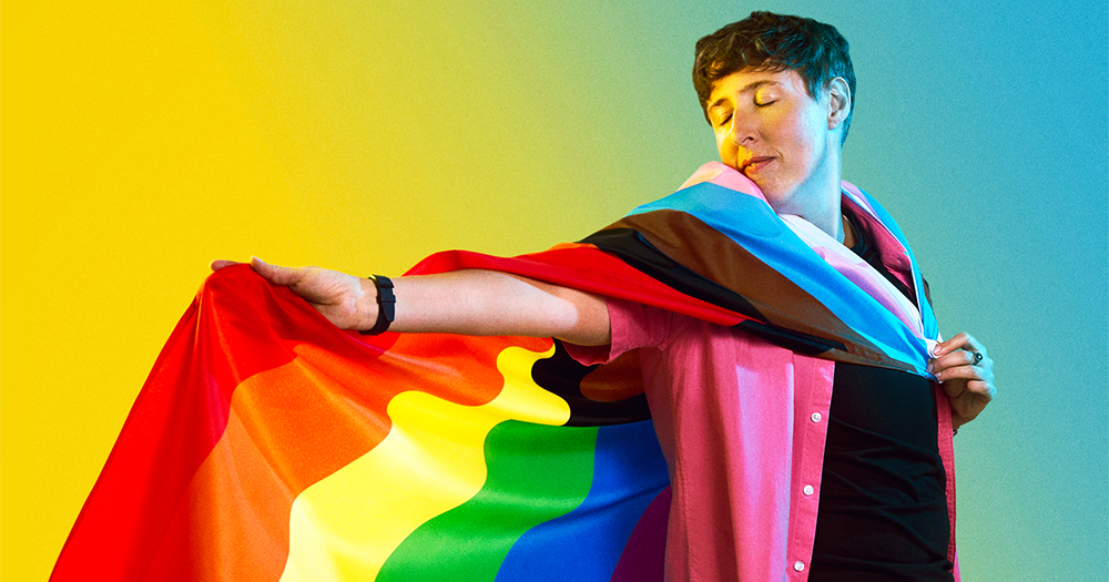 coming out trans: portrait of trans man Adam draped in a rainbow flag