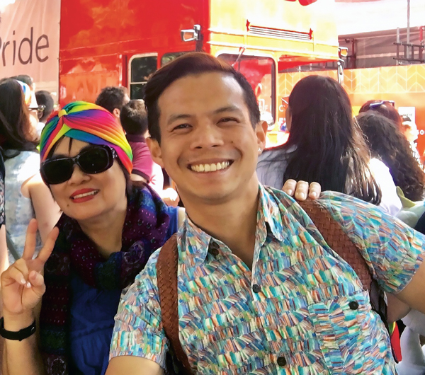 Roberto Sy talks about coming out in the workplace - In the photo, a smiling man, behind him a woman wearing a rainbow headband and sunglasses.