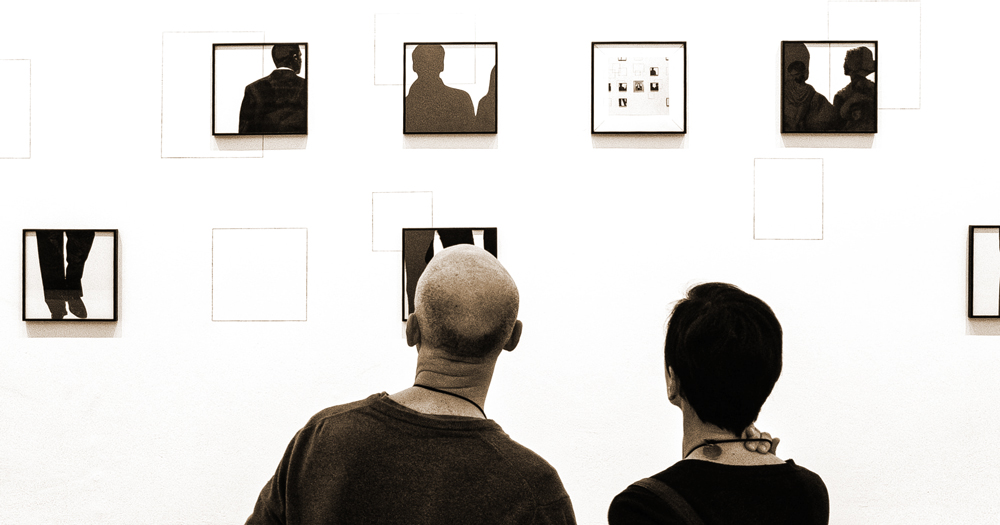 Two people looking at small framed images in a gallery