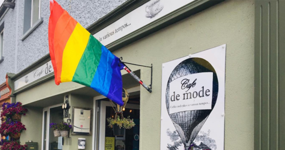 A rainbow flag hanging on the outside wall of a cafe