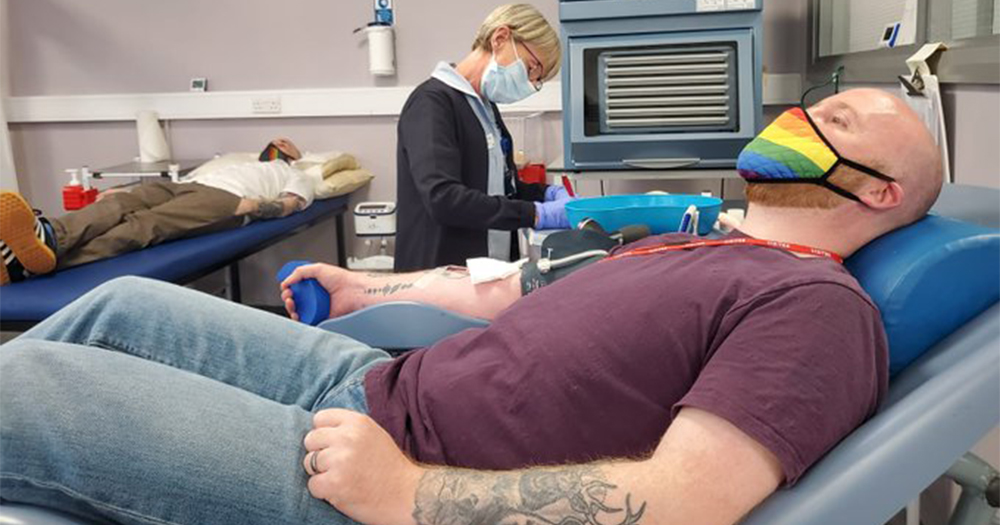 Two men giving blood in a clinic while nurse stands by