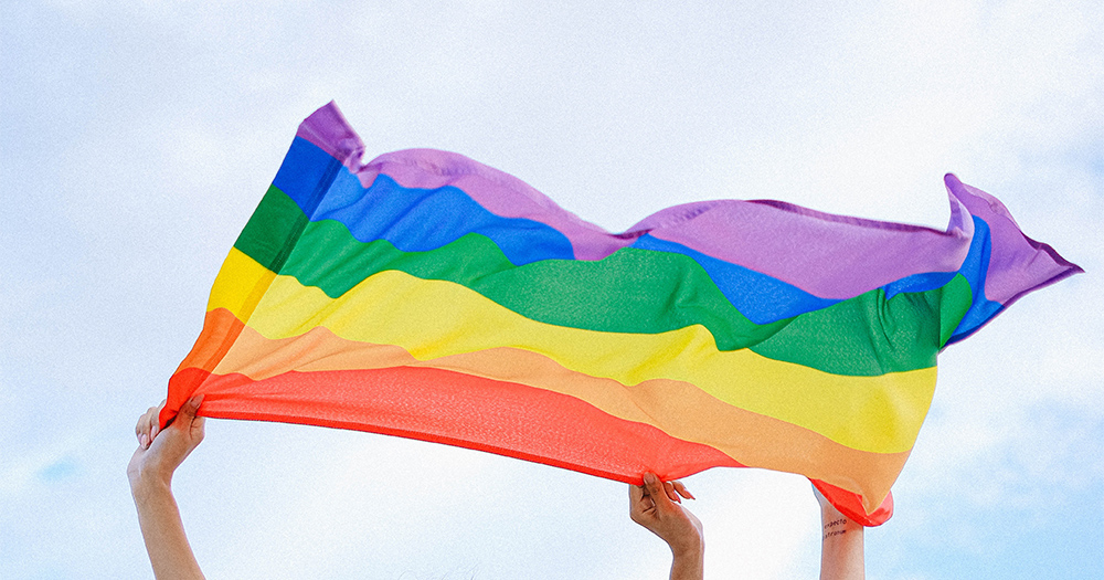 Hands holding up a Pride flag in the wind