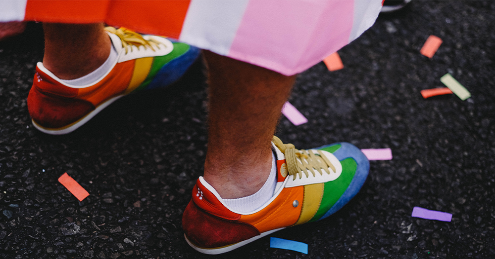 Feet wearing rainbow coloured trainers surrounded by confetti on the ground