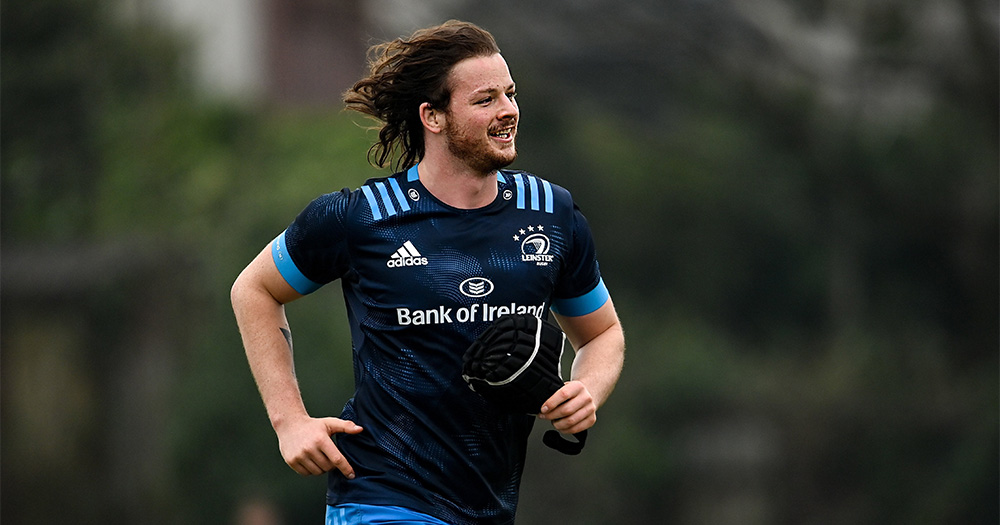 A smiling long haired man in rugby gear running