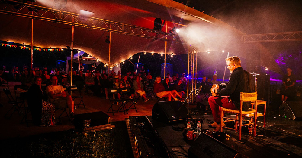 SoFFT Nights promo shot: A man playing an accordion onstage in a tent with people watching
