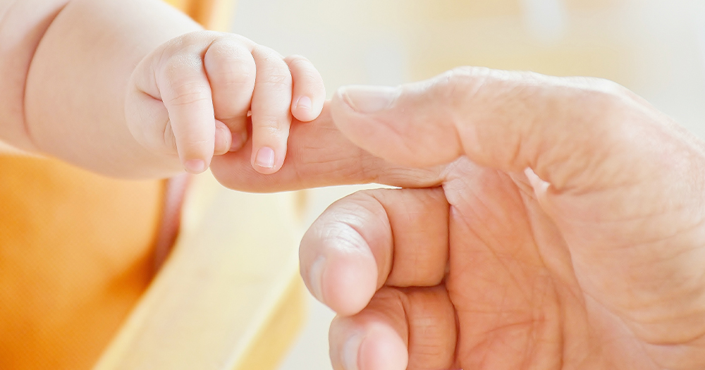 A baby's hand holding a man's finger