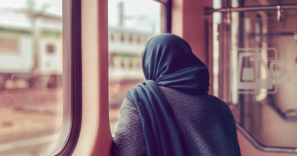 an image of a woman staring out a window wearing a hijab