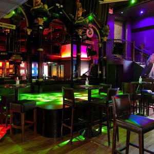 Empty interior of The George, colourfully lit stage surrounded by vacant chairs and tables