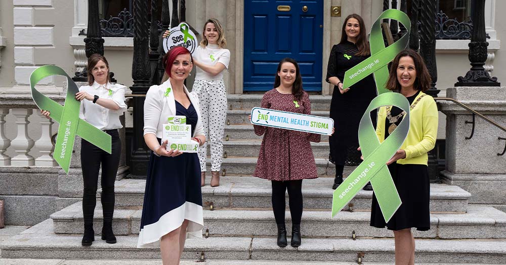 A group of women holding giant green ribbons on the steps of a building