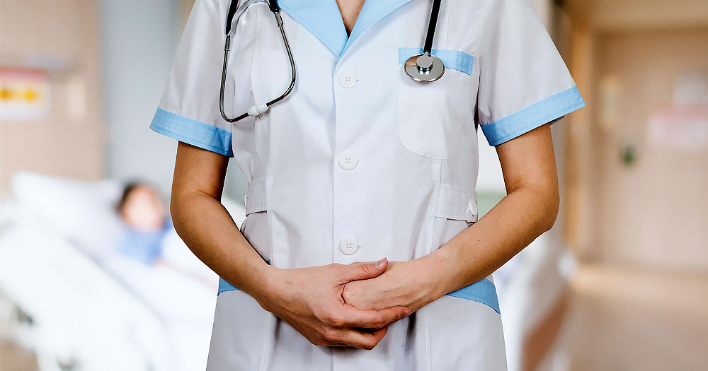 Close up of doctor's midsection, stethoscope draped over shoulders, hands clasped in front of stomach
