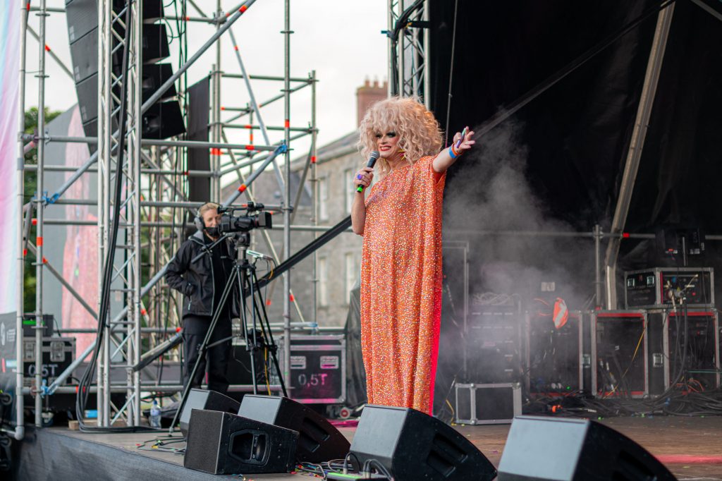 Panti hosting the main stage of the Block Party wearing an orange kaftan with her arms aloft