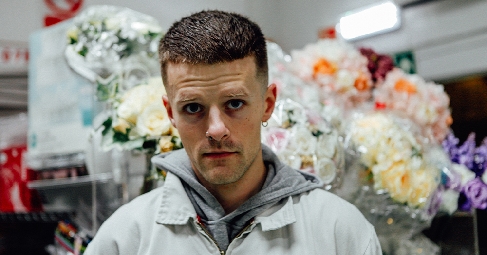 A man surrounded by bouquets of flowers in plastic looks into the camera