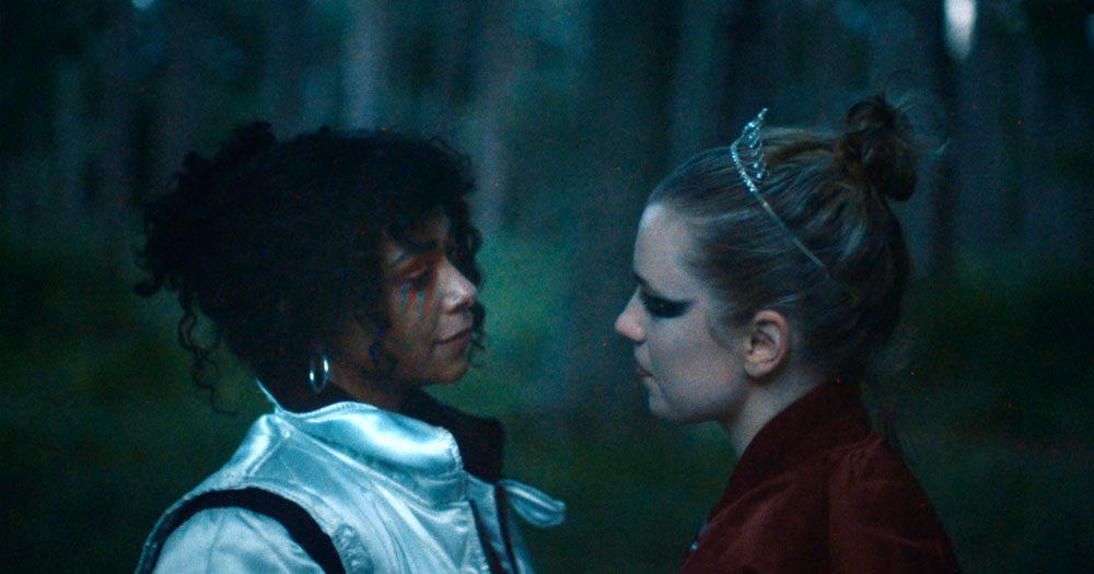 Video still from latest Elaine Mai single, two women in a forest looking at each other lovingly
