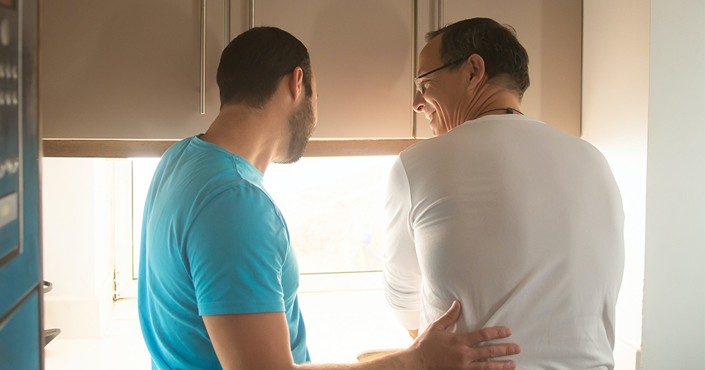 A younger man putting his hand on an older man's back in a kitchen