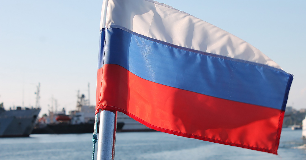 Close-up of the Russian flag, boats can be seen in the background. Russia has proposed to label LGBTQ+ groups as extremist.