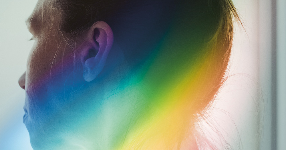 A woman seen from behind with her hair pinned up and a rainbow light shining on her