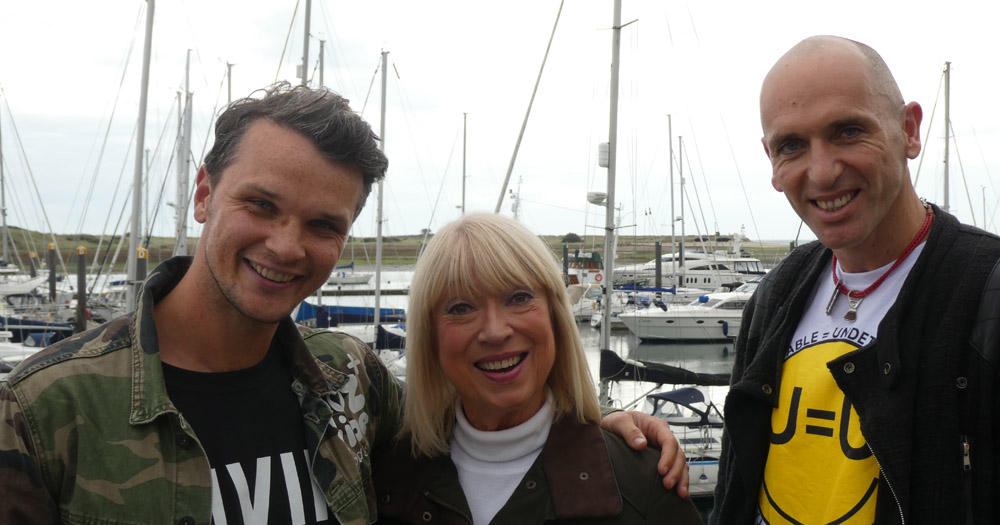 Poz Vibe Podcast crew - Robbie Lawlor (left), Anne Doyle (middle), and Veda Lady (right). They are standing in front of a marina of boats.