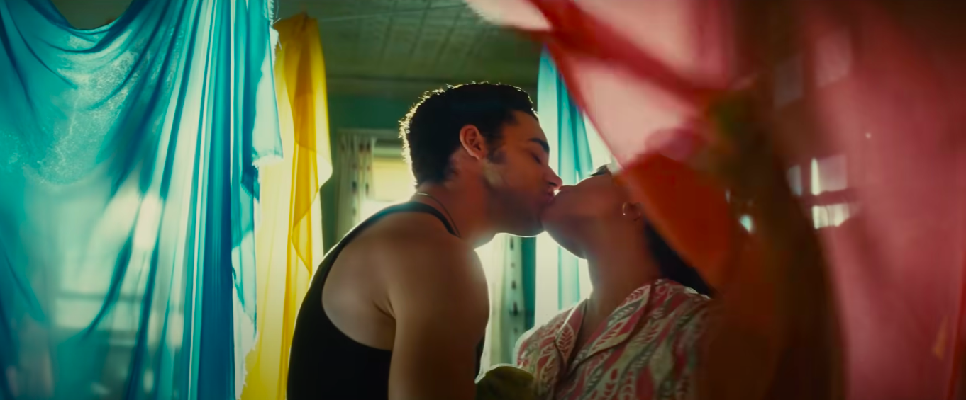 Man and woman are kissing amidst pink, blue, and yellow sheer curtains. This is a scene from the new musical West Side Story.