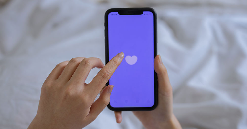 Someone is tapping on their iPhone with a purple screen and white heart. Grindr is fined in Norway after it violates data privacy.
