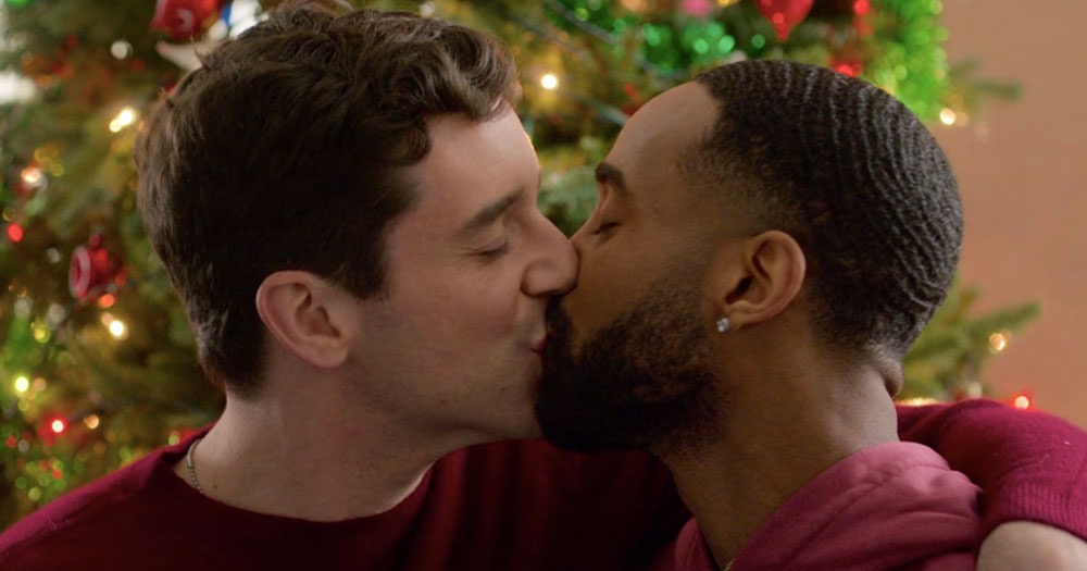 Two men kissing in front of a Christmas tree. New LGBTQ+ Christmas films to cheer for this holiday season.