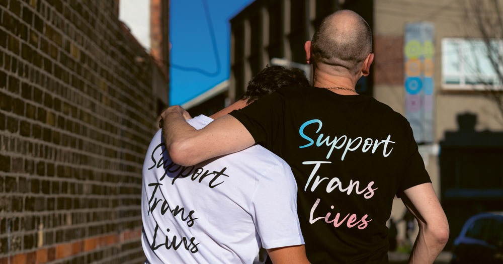 Image of Poz Vibe podcast Veda and Robbie in colourful jacket emblazoned with the text support trans lives