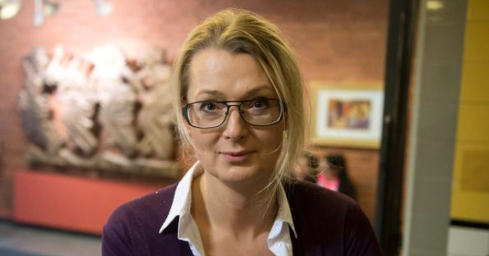 Photograph of new Swedish Trans minister, Lina Axelsson Kihlblom - Head shot of a woman wearing a purpule jacket with a white shirt. She has blonde hair and glasses.