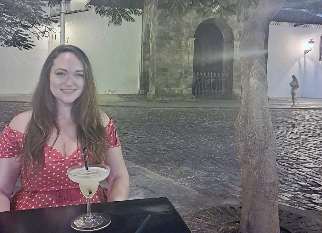 a woman sits at a table on her holiday with a cocktail in front of her