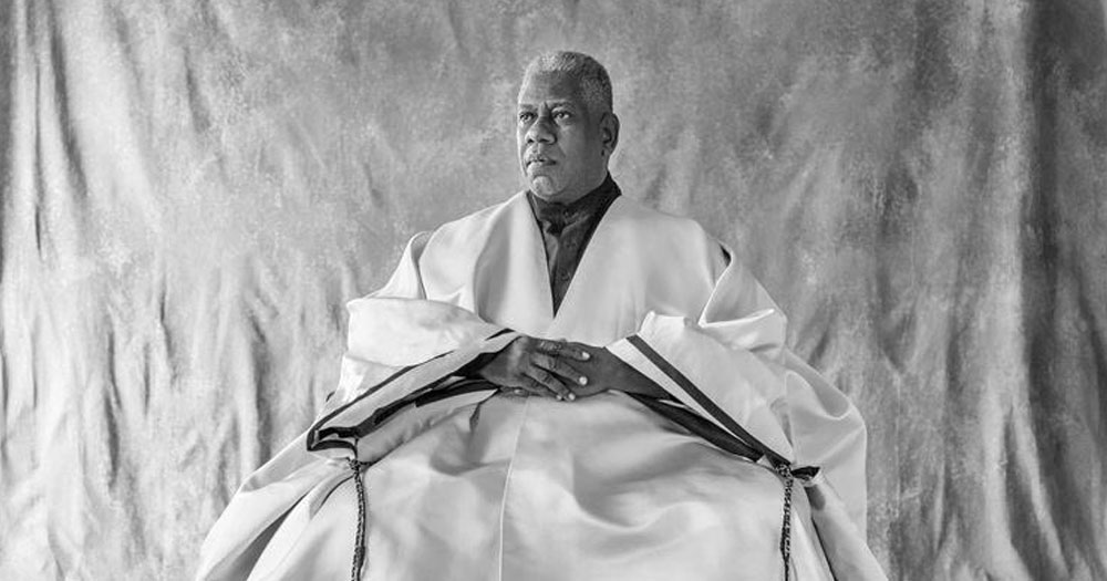 Black and white photo of André Leon Talley sitting and wearing a large flowy garment with his hands clasped in his lap
