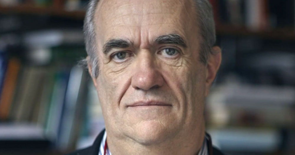 Close up of Colm Tóibín with books and bookshelves in the background